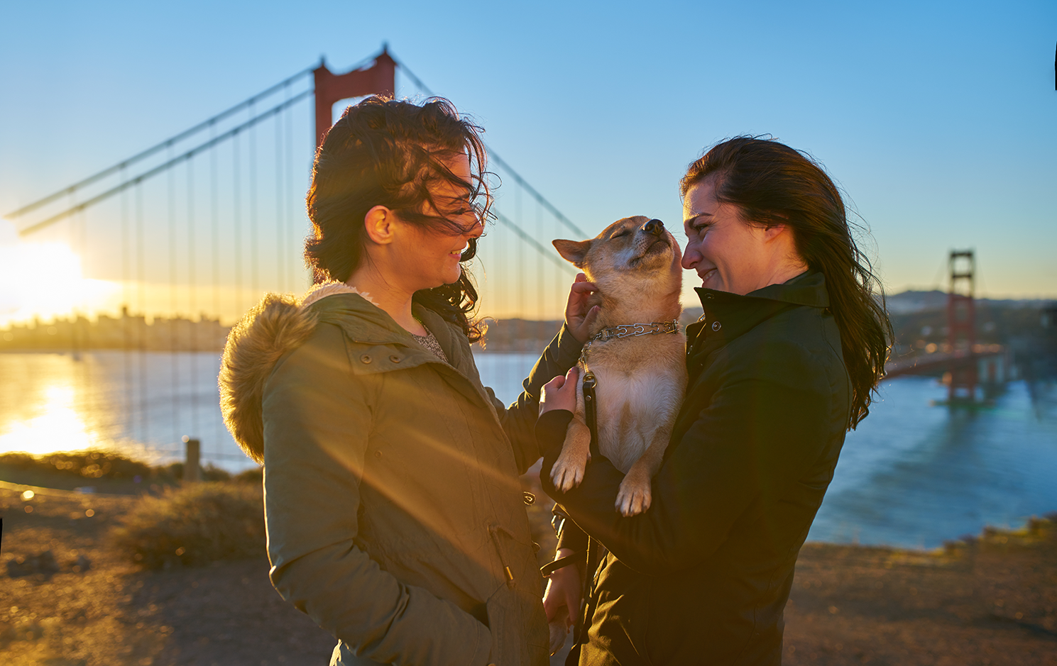 Dog with her 2 owners behind San Francisco's The Golden Gate Bridge