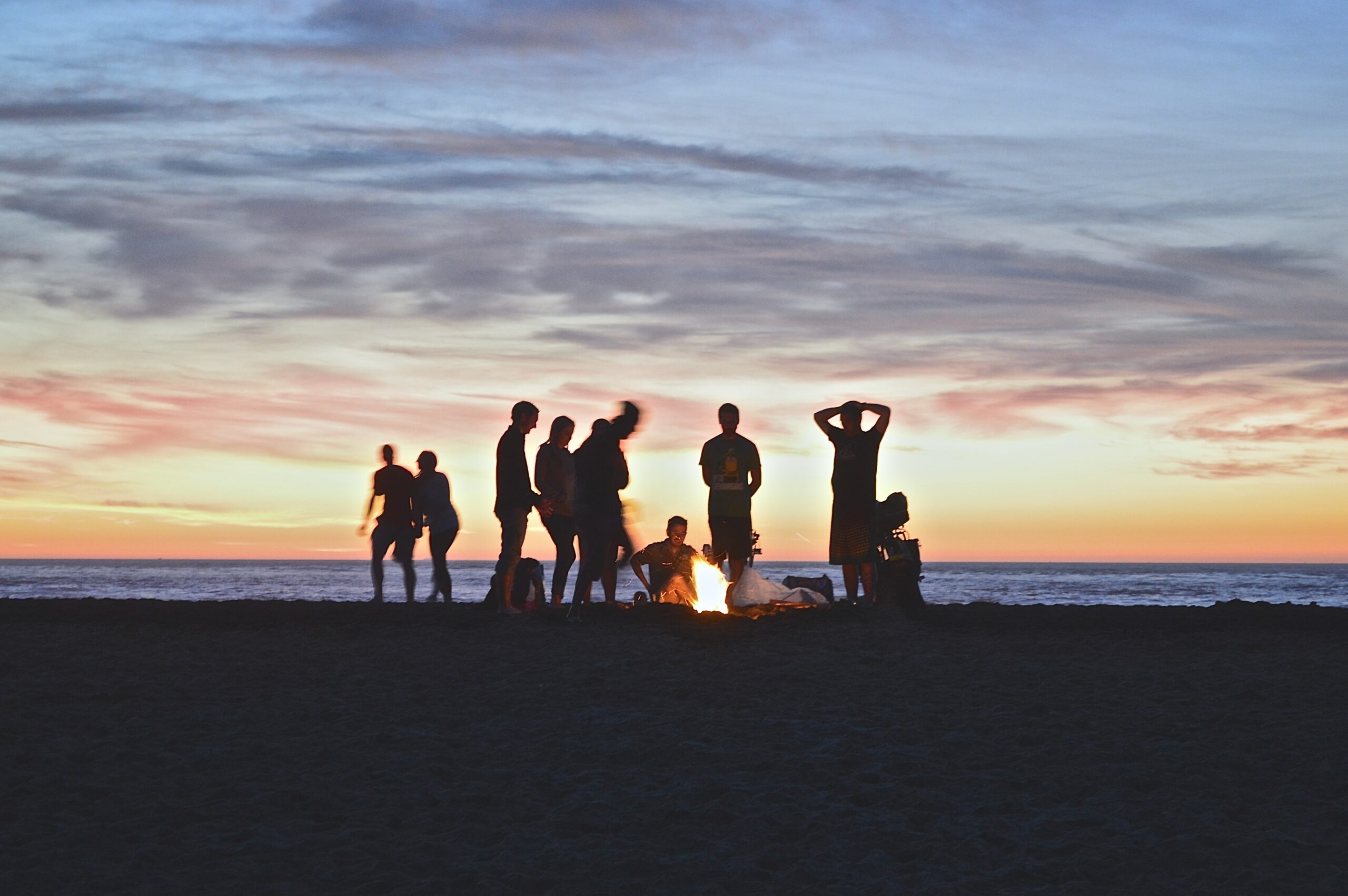 A silhouette of group of people setting up campfire by the beach